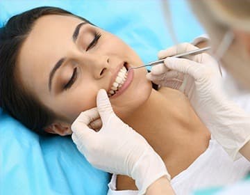 Dentist examining a smiling patient’s teeth with a dental mirror and probe during a routine checkup.